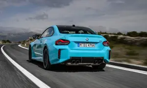 Błękitne BMW M2 z czterema końcówkami wydechu pędzi po krętej drodze w górach.