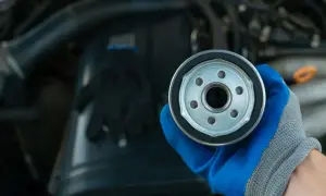 Nowy filtr oleju do silnika 1.6 TDI. Ręka w niebieskiej rękawicy trzyma filtr.