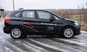 Czarne BMW F45 z logo BMW TEAM Długołęka stoi na mokrej drodze. W tle przejazd kolejowy i pola.