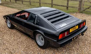 Czarny Lotus Esprit Turbo z czerwonym wnętrzem, zaparkowany na żwirze, z charakterystycznymi żaluzjami na tylnej szybie.