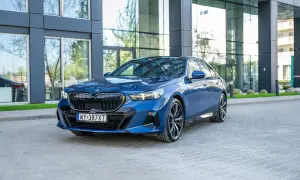 Eleganckie, granatowe BMW 540d z nowoczesnym designem, zaparkowane przed szklanym budynkiem.