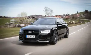 Czarny Audi RS8 pędzi po krętej drodze, mijając malowniczą wioskę.