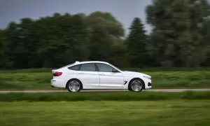 Białe BMW 330d mija zielone pola i drzewa, poruszając się z dużą prędkością.