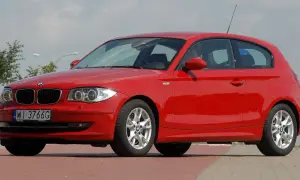 Czerwone BMW E81 z polskimi tablicami WI 3766G zaparkowane na czerwonym podjeździe.