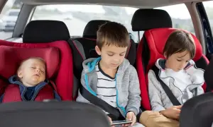 Maluch śpi w foteliku, starsi bracia grają na telefonach. Od kiedy dziecko może jeździć bez fotelika, zależy od jego wzrostu i wagi.
