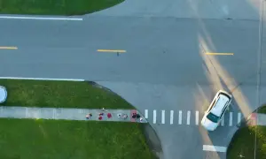 Grupa ludzi czeka na przejściu dla pieszych na skrzyżowaniu z drogą podporządkowaną. Samochód zbliża się do przejścia.