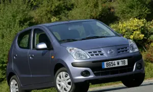 Niebieski Nissan Pixo z tablicą rejestracyjną 8654 W 78 na tle zieleni.