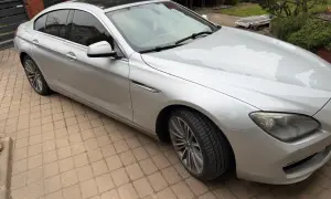 Srebrne BMW 640i z czarnym dachem stoi na podjeździe z kostki brukowej.