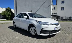 Biała Toyota Corolla 2017 zaparkowana na placu przed budynkiem.