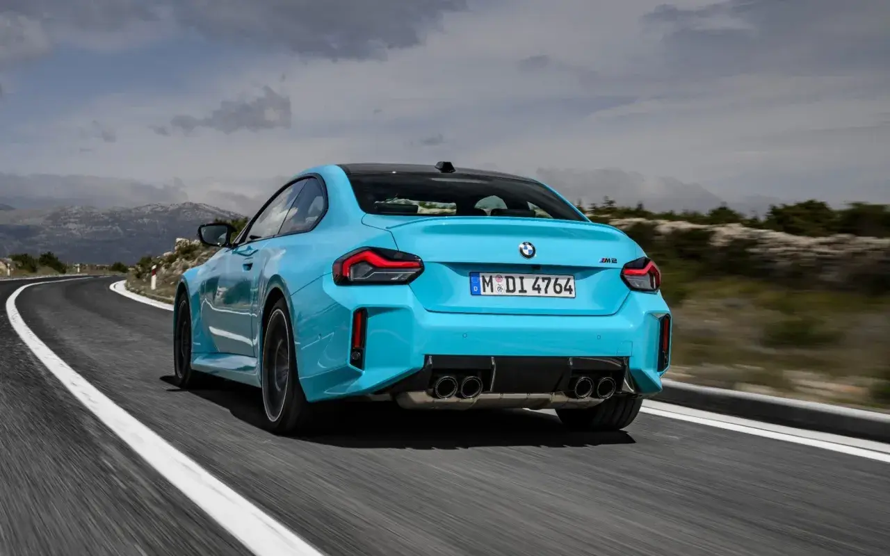 Błękitne BMW M2 z czterema końcówkami wydechu pędzi po krętej drodze w górach.