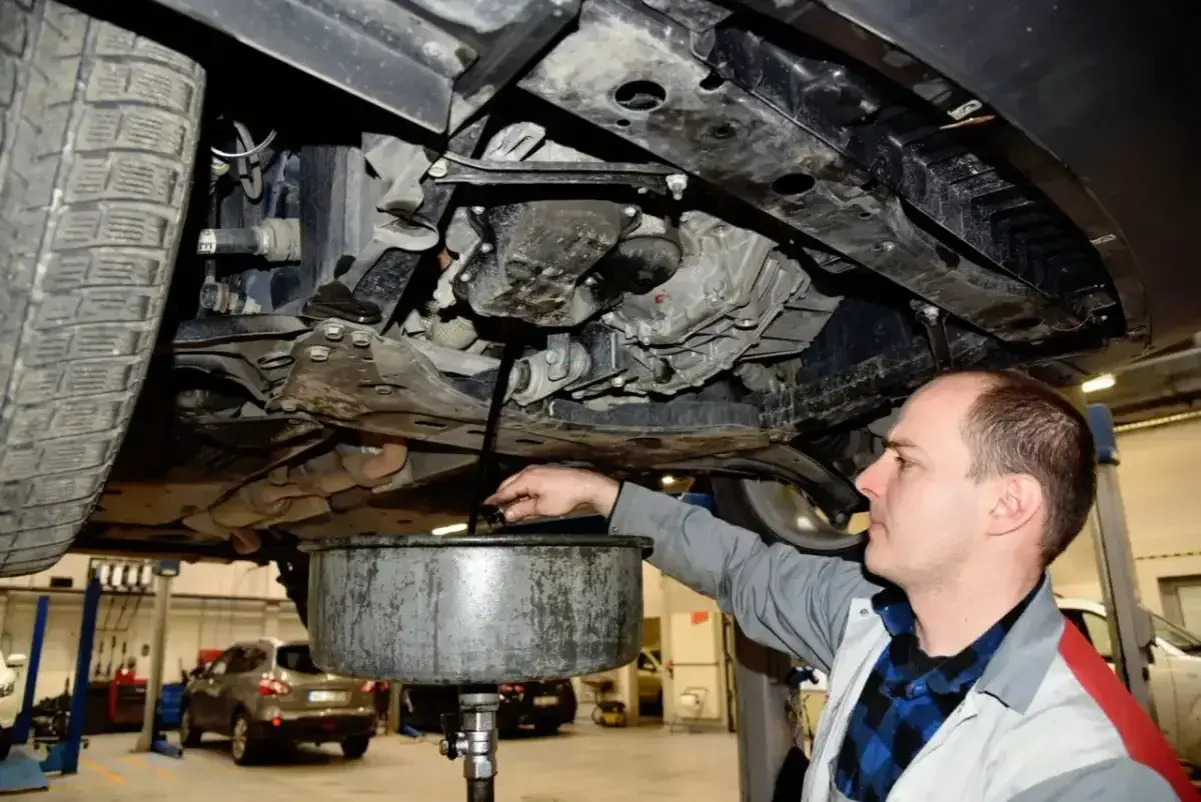 Mechanik spuszcza olej z silnika samochodu. Pamiętaj o regularnej wymianie oleju, by auto służyło Ci długo.