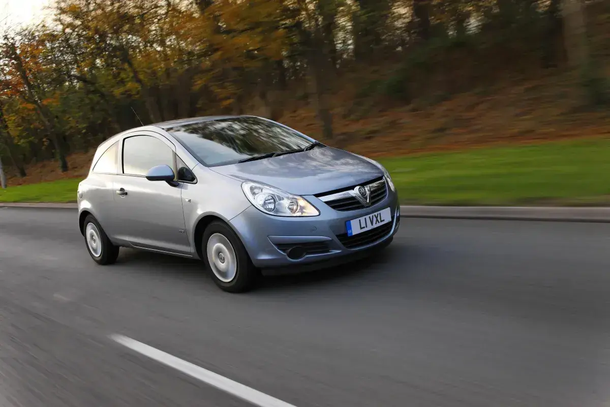 Srebrny Opel Corsa D 1.2 benzyna w ruchu, z rozmytym tłem jesiennego lasu.