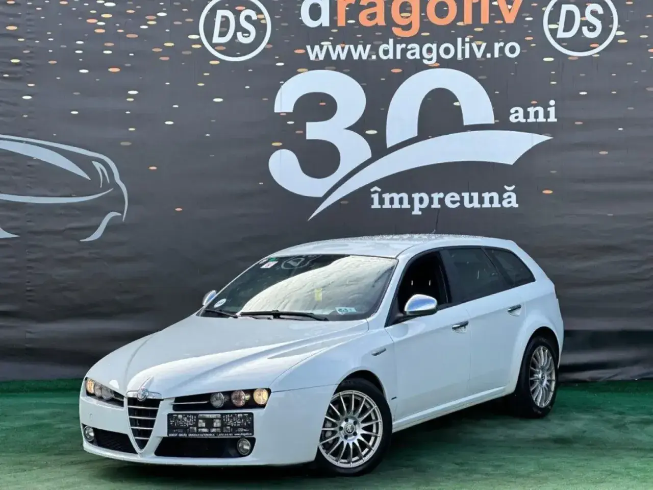 Białe Alfa Romeo 159 1.9 JTD kombi na tle baneru z napisem "30 ani împreună".