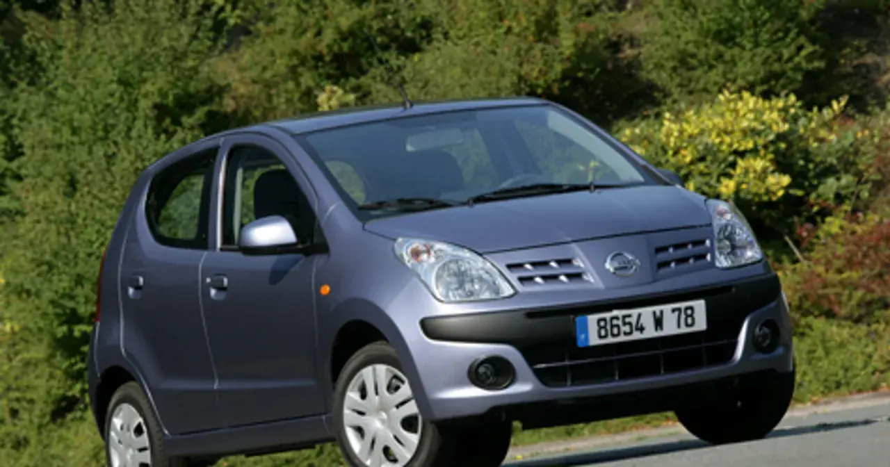 Niebieski Nissan Pixo z tablicą rejestracyjną 8654 W 78 na tle zieleni.