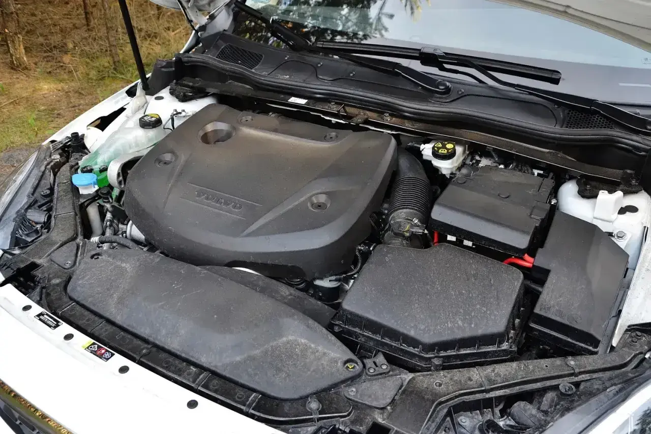 Silnik D2 w Volvo V40, gotowy do pracy. Widać osłonę silnika z logo Volvo, skrzynkę bezpieczników i elementy układu dolotowego.
