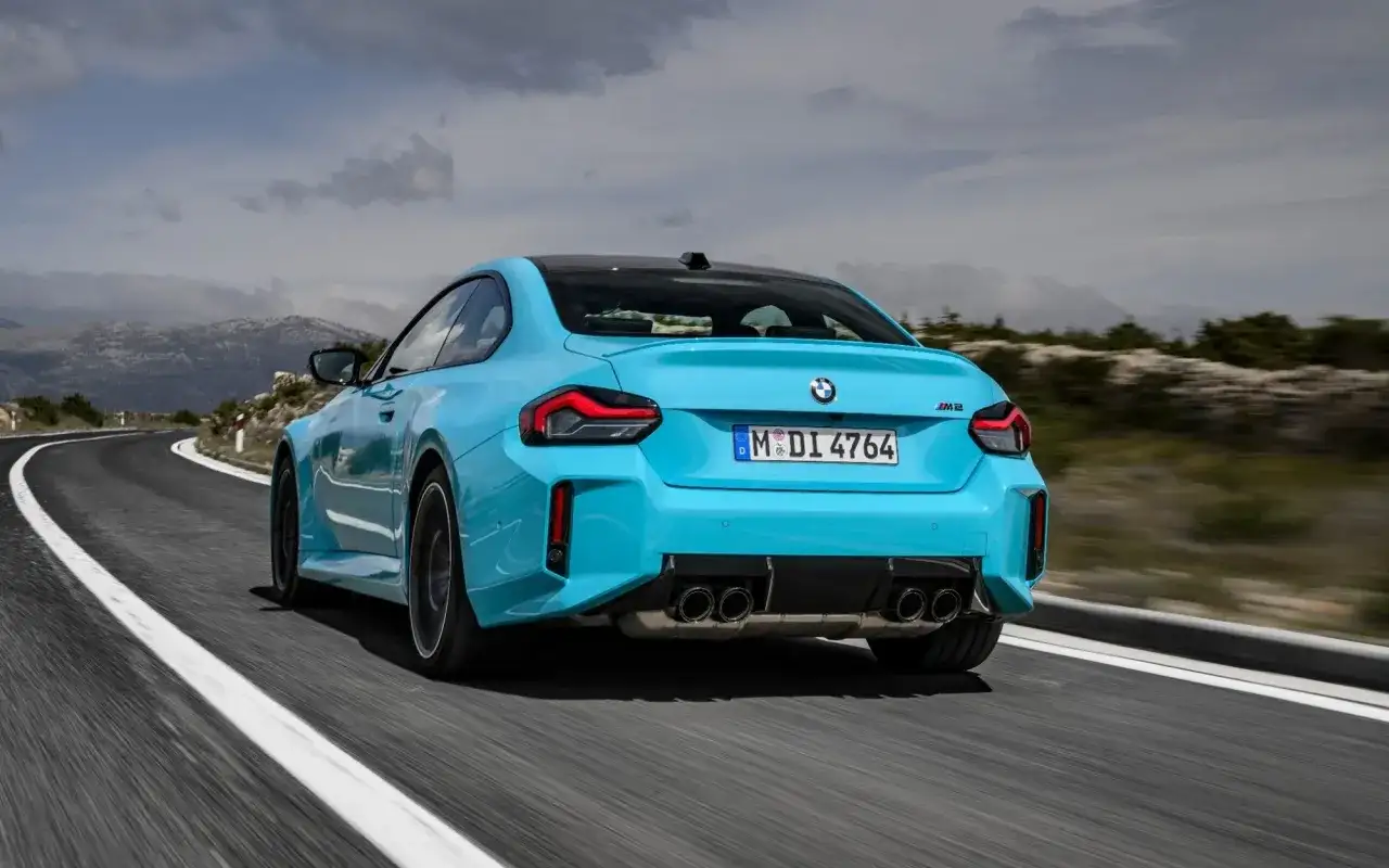 Błękitne BMW M2 z czterema końcówkami wydechu pędzi po krętej drodze w górach.