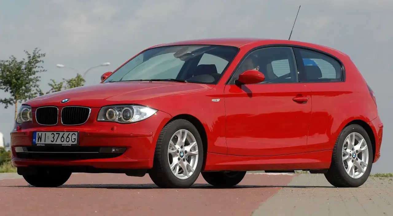 Czerwone BMW E81 z polskimi tablicami WI 3766G zaparkowane na czerwonym podjeździe.