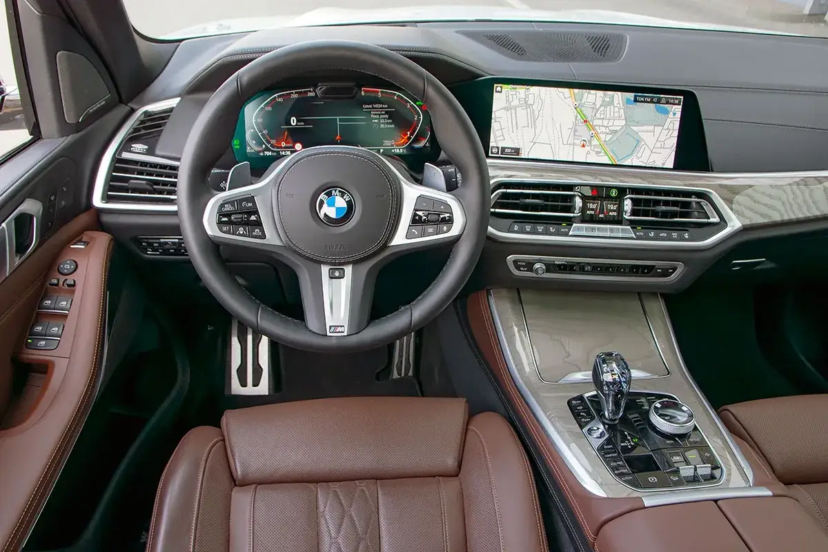 Wnętrze BMW G05 z brązową skórzaną tapicerką, cyfrowymi zegarami i ekranem nawigacji.