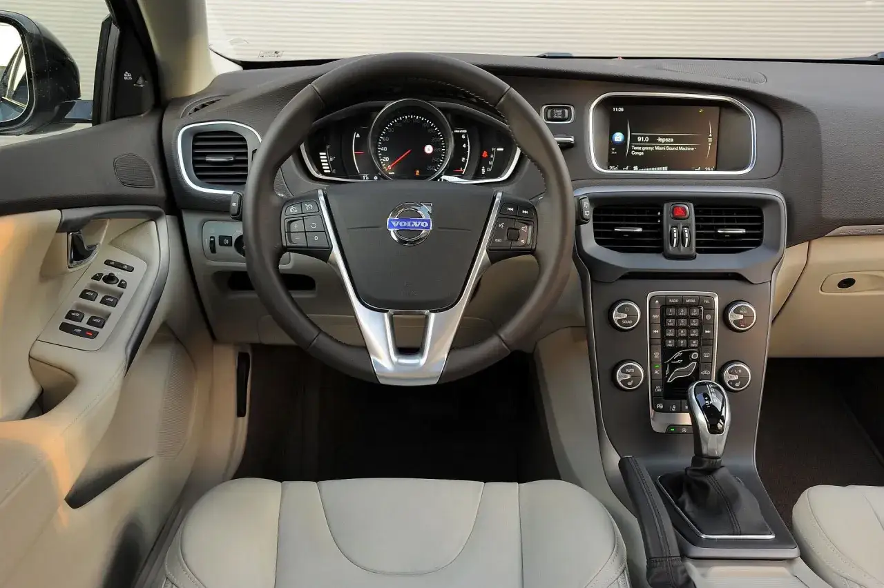 Wnętrze Volvo V40 2015: kierownica, deska rozdzielcza z ekranem multimediów i panelem sterowania, dźwignia zmiany biegów.