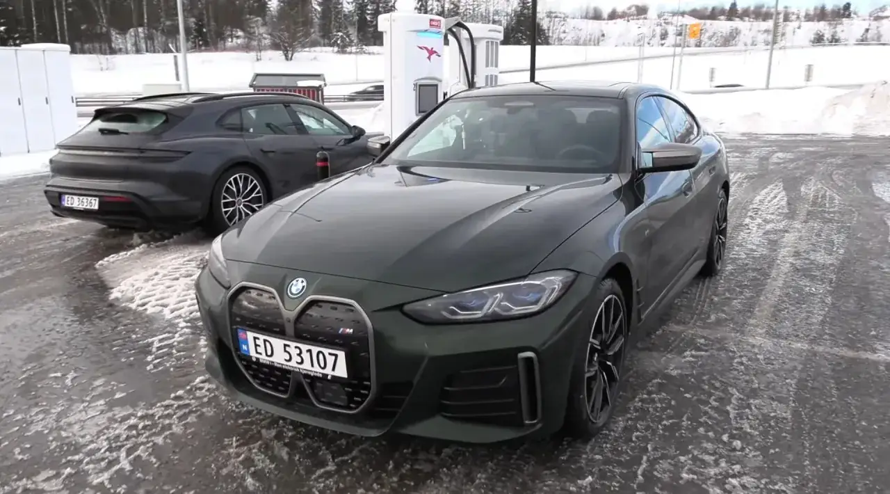 Zielone BMW i4 stoi na ładowarce obok Porsche Taycan. Zimowy krajobraz i mokra nawierzchnia.