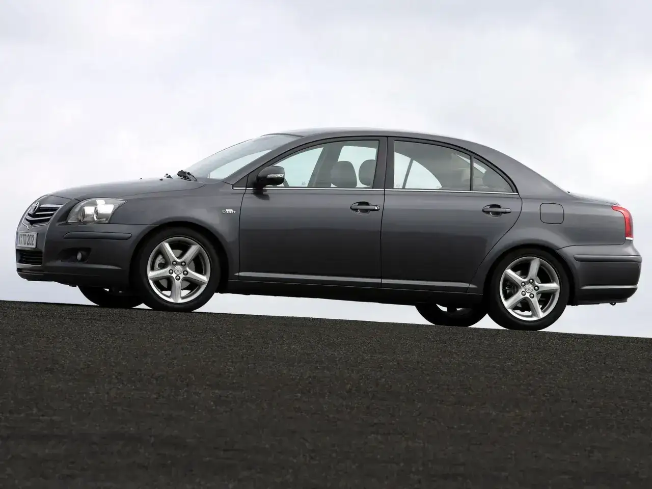 Szary sedan Toyota Avensis T27 1.8 benzyna na tle nieba.