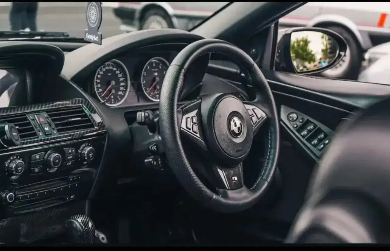 Wnętrze BMW E64 z czarną kierownicą, deską rozdzielczą i karbonowymi wstawkami.