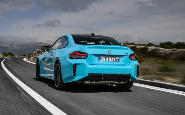 Błękitne BMW M2 z czterema końcówkami wydechu pędzi po krętej drodze w górach.
