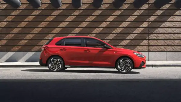 Czerwony Hyundai i30 Hatchback zaparkowany na tle ceglanej ściany z geometrycznymi cieniami.