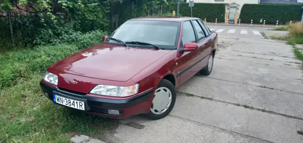 Czerwony Daewoo Espero z tablicą rejestracyjną WN 3841R stoi na betonowej drodze obok zielonego trawnika.