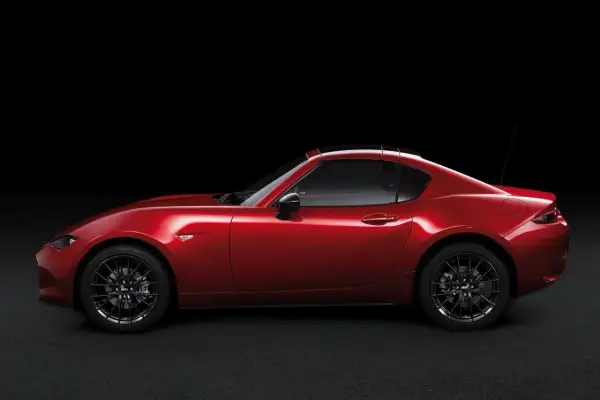 Czerwona Mazda MX-5 RF targa z czarnym dachem, zaparkowana na ciemnym tle.