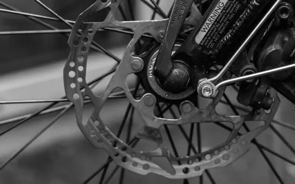 Zbliżenie na tarczę hamulcową i szprychy roweru. Widoczny mechanizm szybkiego zwalniania Shimano i ostrzeżenie. RWD.
