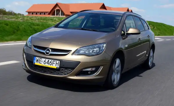 Brązowy Opel Astra J hatchback w ruchu drogowym, z charakterystycznym grillem i reflektorami.