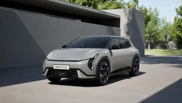 Nowy Kia EV4 GT-Line w kolorze srebrnym, zaparkowany przed nowoczesnym budynkiem z zielenią w tle.