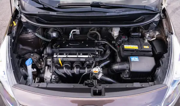 Silnik Kia Rio 3 z widocznym akumulatorem, przewodami i innymi elementami układu napędowego.