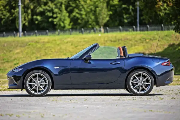 Granatowy roadster z brązowymi zagłówkami, zaparkowany na tle zielonej skarpy i drzew.