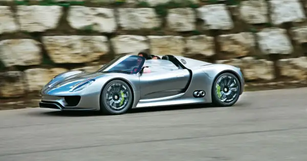 Srebrny Porsche 918 Spyder pędzi po drodze, z kierowcą za kierownicą.