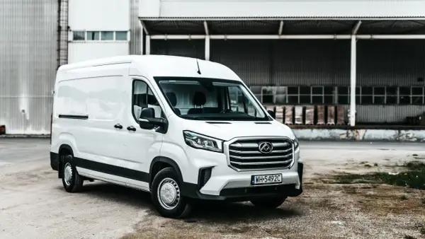 Biały Maxus Deliver 9 stoi przed magazynem. Ten wszechstronny van jest gotowy do pracy, przewożąc towary z miejsca na miejsce.