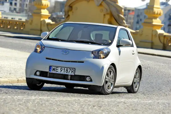 Biały, kompaktowy samochód Toyota iQ z polskimi tablicami WE 9187R jedzie po moście. Ten model, choć nie jest Daihatsu, oferuje podobną zwinność w mieście.