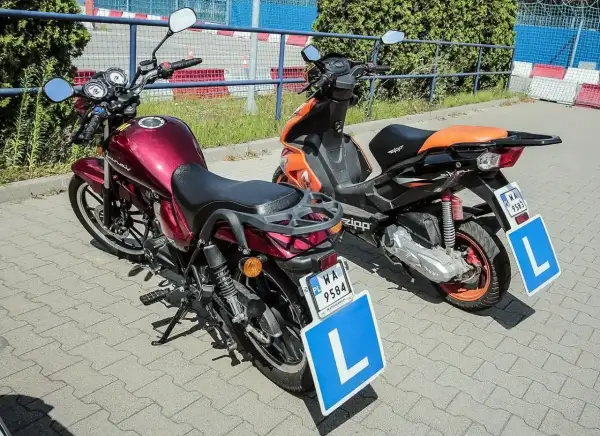Dwa motorowery z tabliczkami "L" na postoju. Od ilu lat można jeździć motorowerem? Od 14 lat z kartą motorowerową.