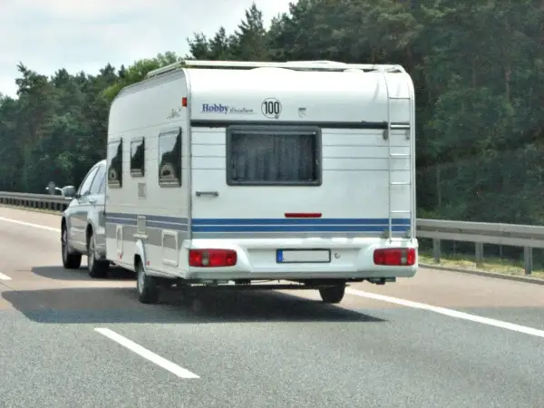 Biała przyczepa kempingowa Hobby jedzie autostradą. Kierowca z kod 96 prawo jazdy wiezie rodzinę na wakacje.