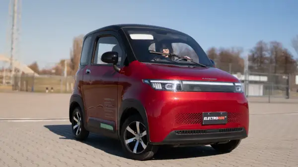 Czerwony, miejski pojazd elektryczny kategoria AM, z kobietą za kierownicą, zaparkowany na zewnątrz.