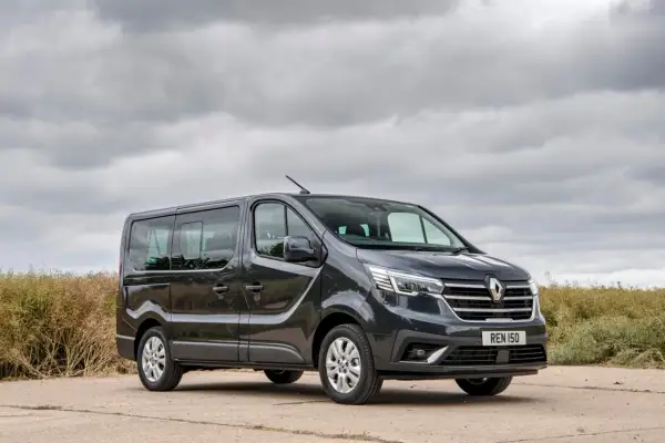 Ciemnoszary Renault Trafic, najmniej awaryjny van 7-osobowy, stoi na tle pochmurnego nieba i zarośli.
