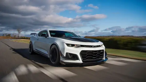 Białe Camaro ZL1 z czarną maską i spoilerem pędzi po torze wyścigowym, zostawiając za sobą rozmyte tło.