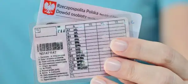 Dłoń trzyma polskie prawo jazdy z widocznymi kategoriami pojazdów, od motocykli po autobusy.