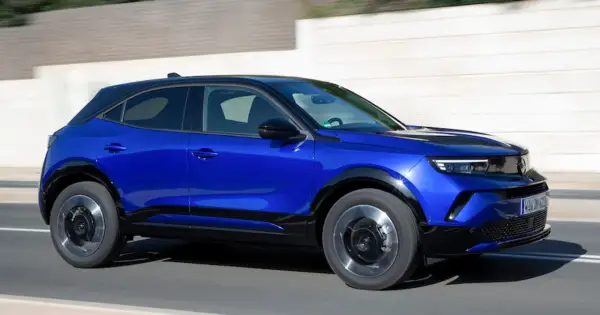 Błękitny Opel Mokka z czarnym dachem pędzi po drodze. Sprawdź aktualną opel mokka cena i wybierz swój wymarzony samochód.