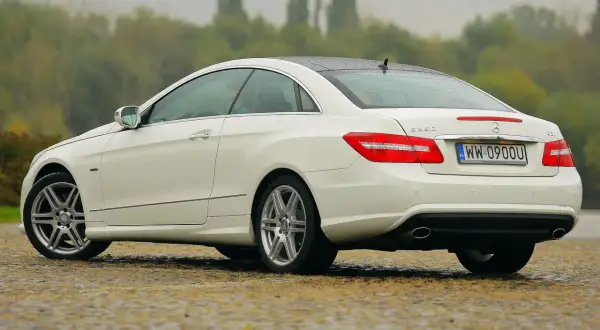 Biały w212 coupe z polskimi tablicami rejestracyjnymi stoi na mokrej nawierzchni.
