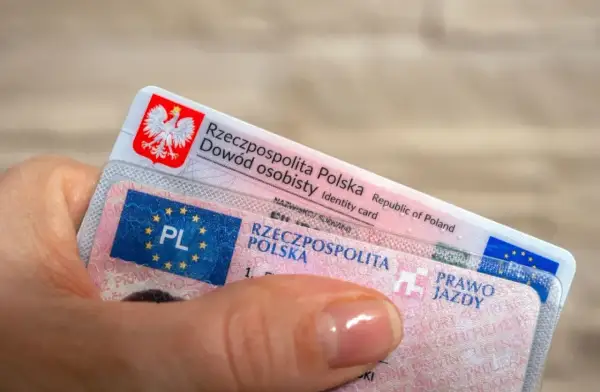 Dłoń trzyma polski dowód osobisty i prawo jazdy. Dokumenty te są niezbędne do poruszania się po drogach, a prawo jazdy bezterminowe daje swobodę na lata.