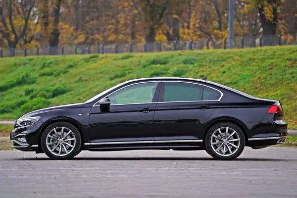 Elegancki, czarny sedan z chromowanymi detalami stoi na tle jesiennego krajobrazu.