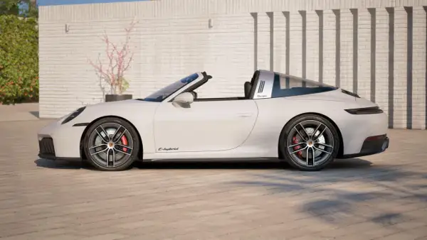 Białe Porsche 911 Targa z otwieranym dachem, z napisem "Targa" na błyszczącym pałąku, stoi na brukowanym podjeździe.
